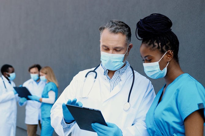 <span>Doctor and nurse have a discussion while reviewing tablet.</span>