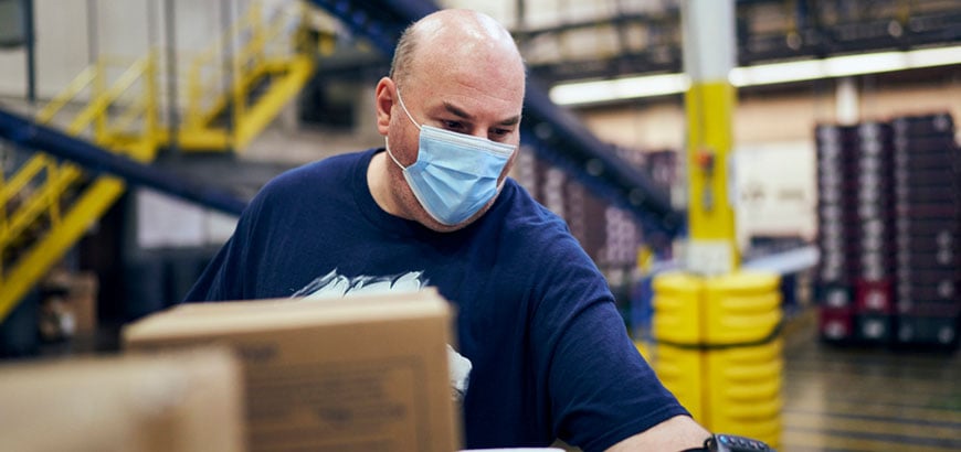 A man with a mask on working inside a distribution center