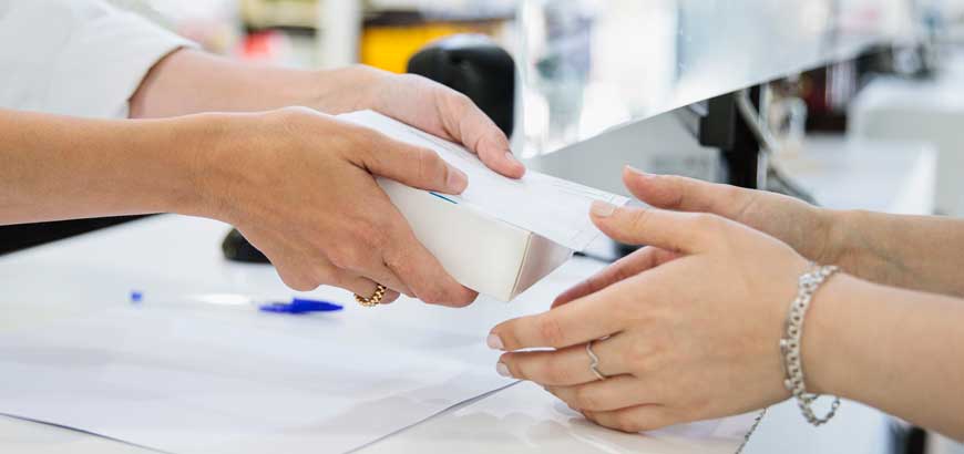 A close up of a pharmacist's hands handing a box of medication to a patients hands.