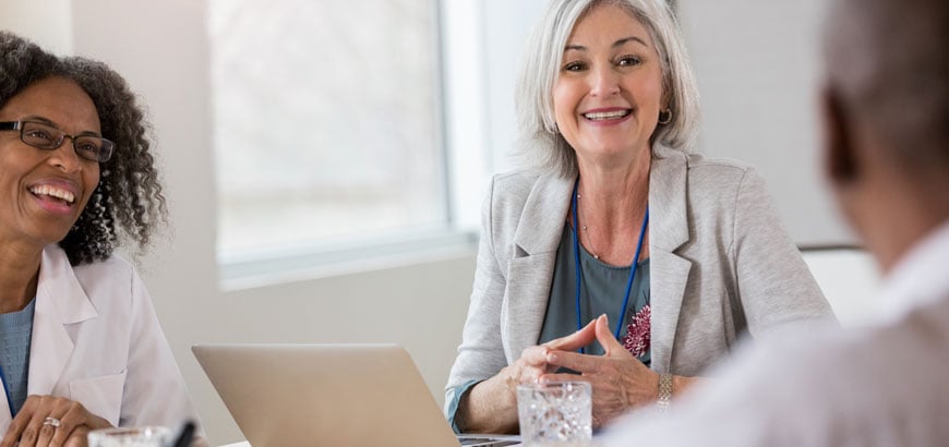 Three hospital executives sit and laugh at a conference table