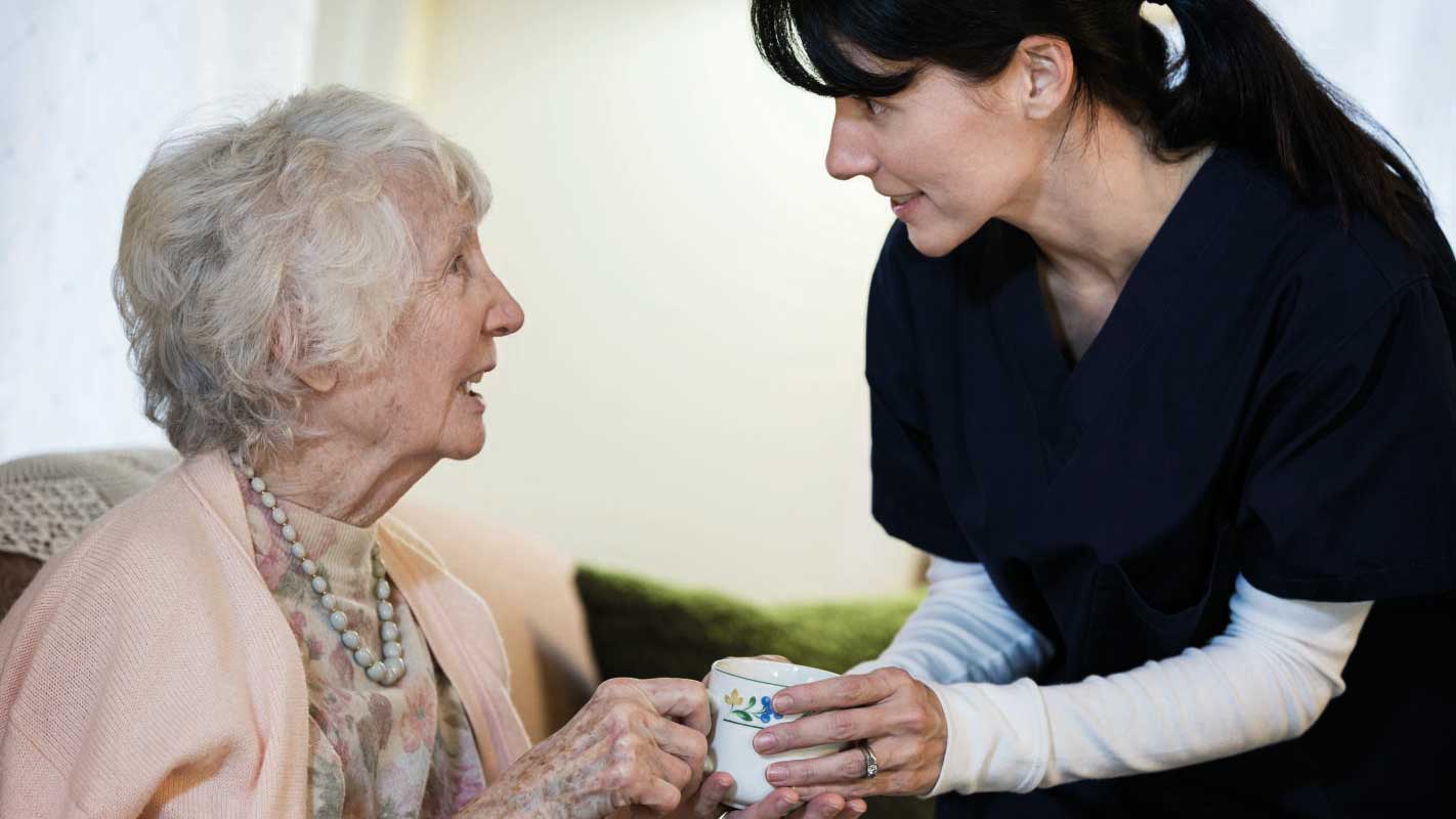 A nurse handing a coffee mug to an elderly woman