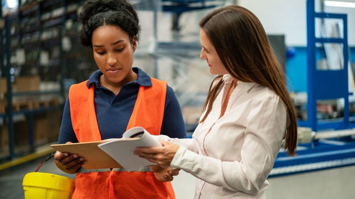 A manager shows a clipboard to a warehouse employee