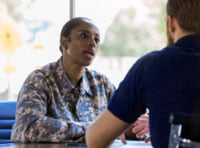 Two people sitting at a table talking, one wears a military uniform