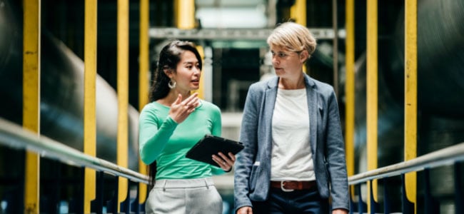 Two women have a conversation while walking and holding a clipboard