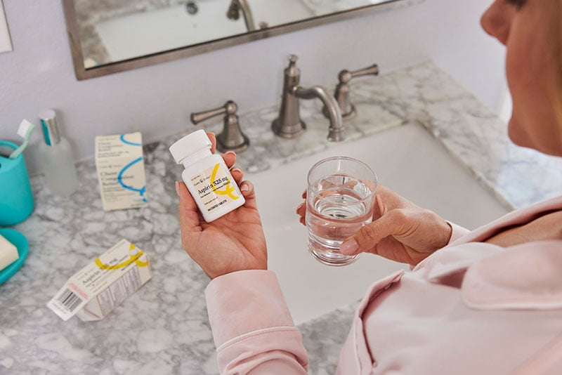 A woman holding a medicine bottle and a glass of water