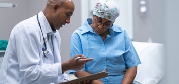 A doctor sits with a patient, holding a clipboard and explaining options