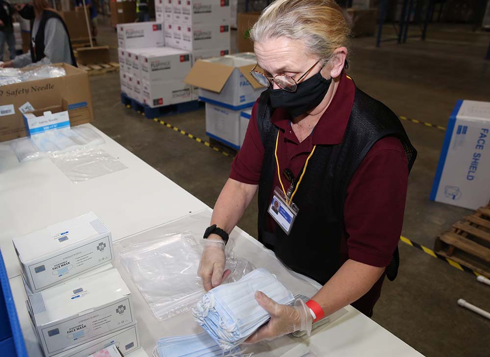 A worker standing at a table holding a stack of medical face masks