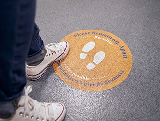 A person standing on a sign on the floor reminding people to stay 6 feet apart